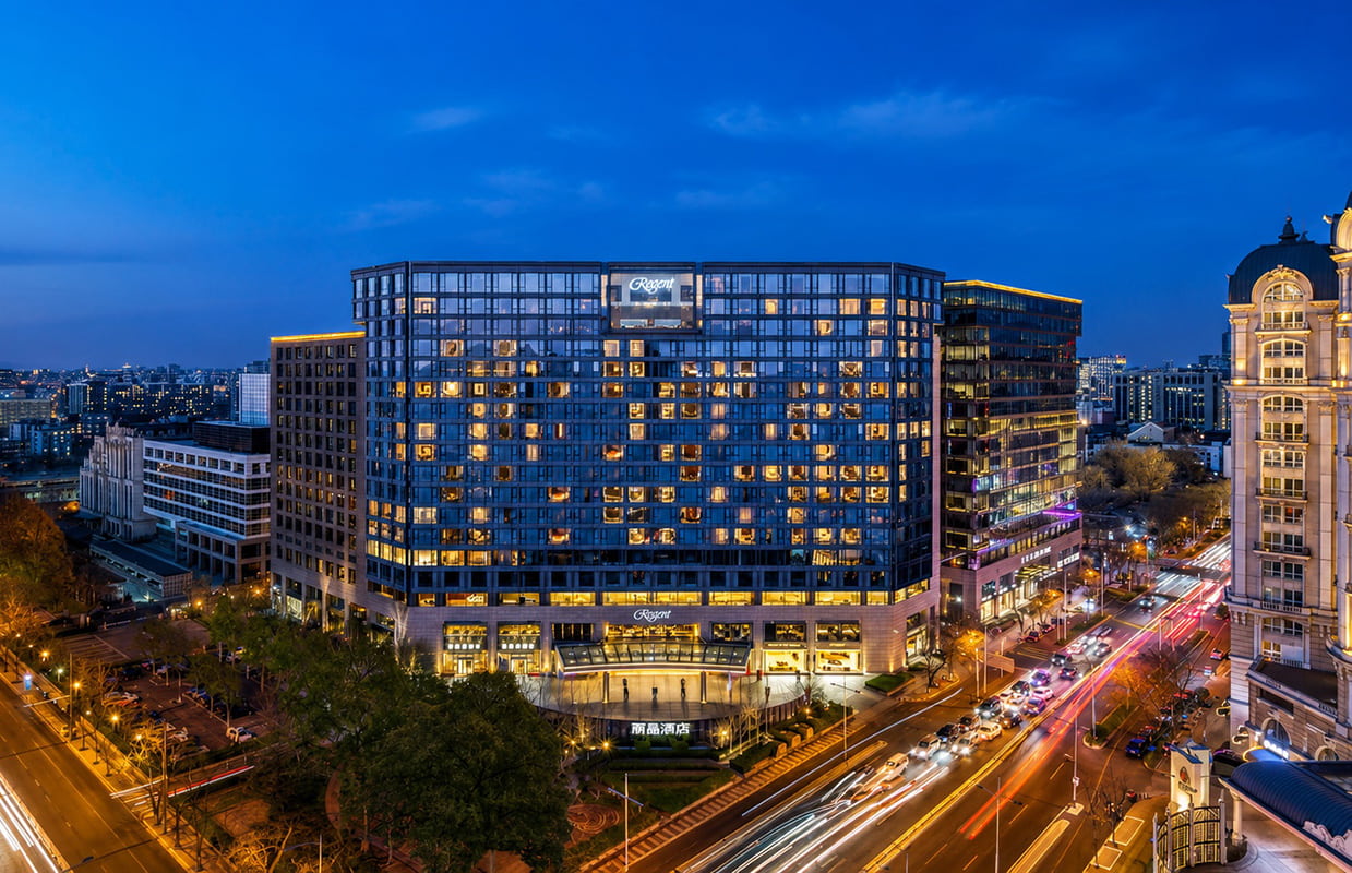 Night view of Regent Beijing luxury hotel with illuminated modern architecture and busy city streets in downtown Beijing, China.